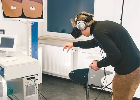 Ein Mann testet zwischen Monitoren und anderen Geräten, mit Kopfhörern und VR-Brille, die Virtual Reality aus.