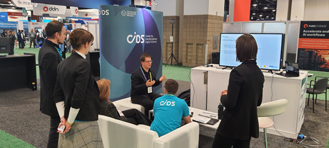Foto während eines Sofa-Talks am gemeinsamen Messestand von ZIH und ScaDS.AI auf der SC23 in Denver. Vortragender und 5 Personen vor einem Monitor.